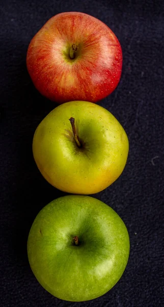 Three apples, one green and two red and yellow on a dark background.