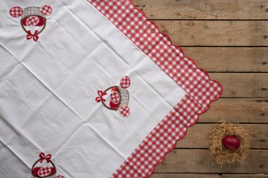 Yuvası ve kırmızı boyalı yumurtası olan ahşap bir yüzey üzerinde paskalya masa örtüsü.