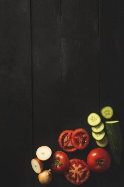 Üzerinde sebzeler, domatesler, salatalıklar ve soğanlar olan siyah ahşap bir arka plan.