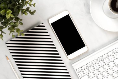 Not defteri, cep telefonu, klavye, fare ve yeşil bir bitkiyle beyaz mermer bir ofis masasına yaklaş