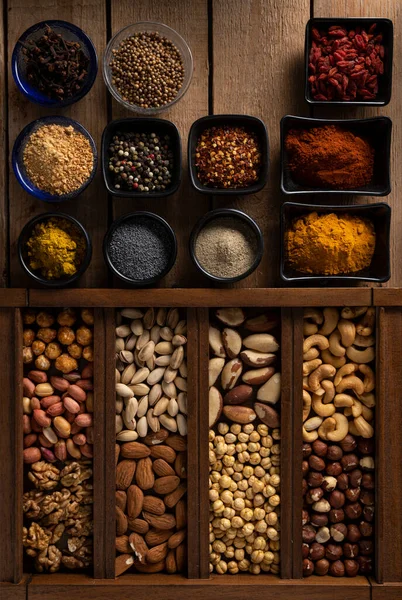 Mix of spices in different shape of bowls and mix of nuts in a wooden box on a wooden surface