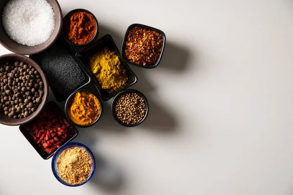 Beyaz arka planda tuzlu, siyah susamlı, haşhaş tohumlu, balkabağı tohumlu, kırmızı biberli, Goji üzümlü, körili, kişniş, Bahari, kakule, sarımsak ve zerdeçal içeren farklı tabaklar.