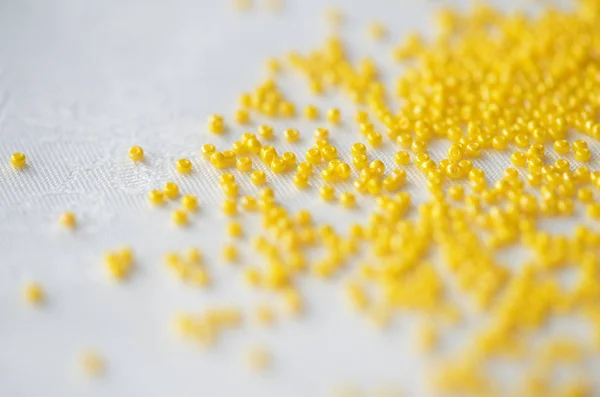 Seed beads of yellow color on textile background close up