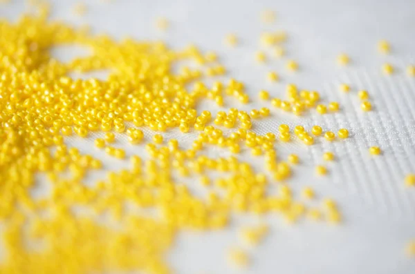 Seed beads of yellow color on textile background close up