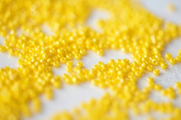 Seed beads of yellow color on textile background close up