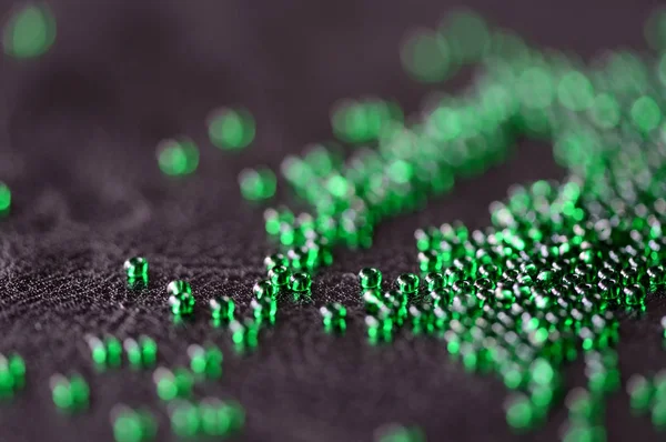 Transparent green seed beads on a dark leather background