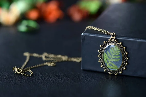 Resin pendant with fern leaf on a dark background close up