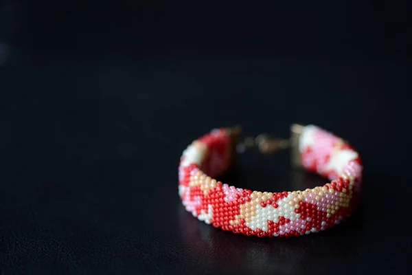 Red camouflage seed beads bracelet on a dark background close up