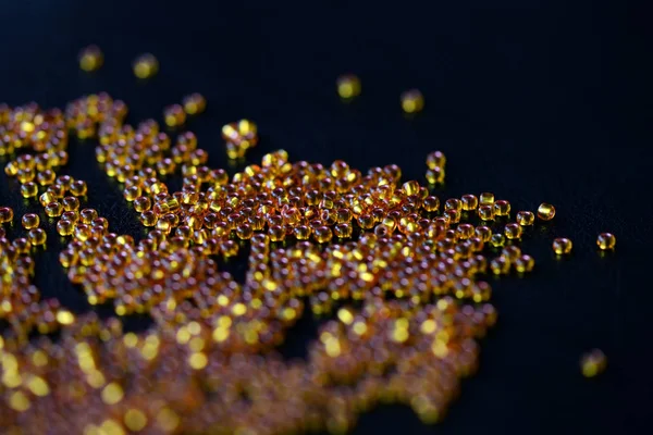 Round yellow seed beads scattered on a dark surface close up