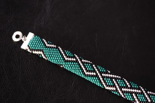 Green bead crochet bracelet with celtic print on a dark background close up