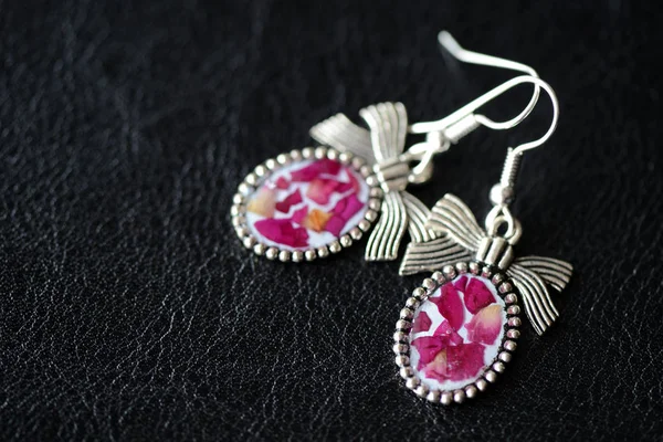 Epoxy resin earrings with dry rose petals on a dark background close up