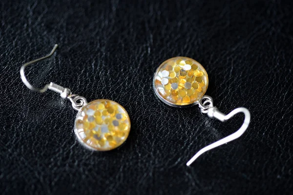 Resin earrings with yellow glitter on a dark background close up