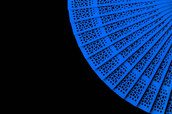 Blue fan with openwork pattern isolated on black background close-up