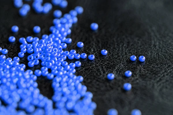 Seed beads blue color scattered on a dark background close up. Handmade and handwork concept