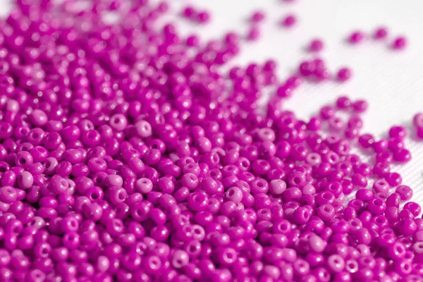 Pink seed beads scattered on a textile surface close up. Handmade background