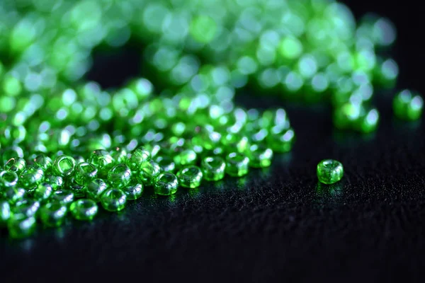 Seed beads green color scattered on a dark background close-up