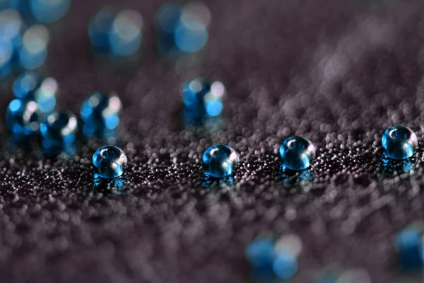 Transparent seed beads blue color scattered on a black leather surface close-up