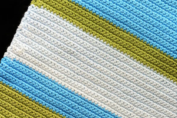 Fragment of crocheted fabric from green, blue and light blue threads close-up, top view. Abstract background. Hand made concept