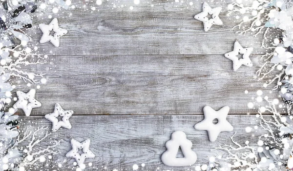Christmas mockup. Frame of white Christmas stars, gingerbreads, twigs, tinsel and snow on white wooden background.