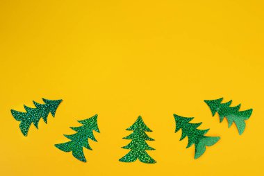 Beş parlak yeşil holografik Noel ağacının eğri olarak dizildiği yaratıcı Noel minimumum sarı renkli maket.. 