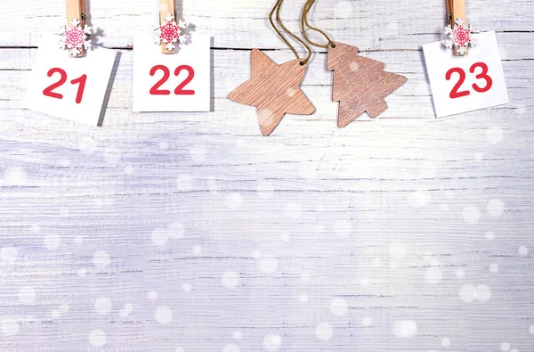 21-23 parte del calendario de Adviento: números en hojas blancas y dos juguetes de Navidad de madera sobre fondo blanco nevado de madera . — Foto de Stock