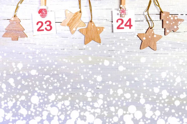 23-24 parte del calendario de Adviento con números en hojas blancas en clips decorativos y juguetes de Navidad de madera sobre fondo blanco nevado de madera con espacio para copiar. Decoraciones navideñas festivas . — Foto de Stock