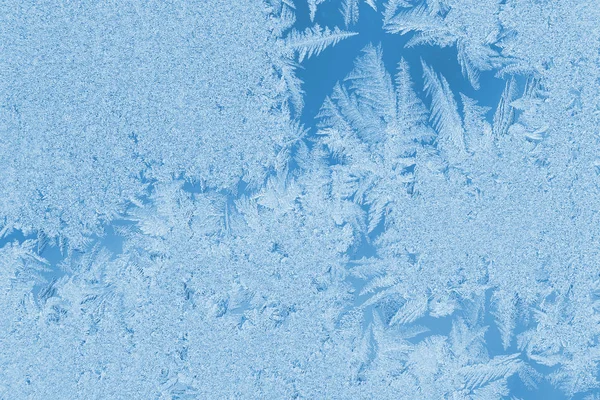 Weihnachten natürlicher Hintergrund in der Trendfarbe 2020 klassisch blau. Winter frostiges Muster bizarre Form auf Fensterglas. — Stockfoto