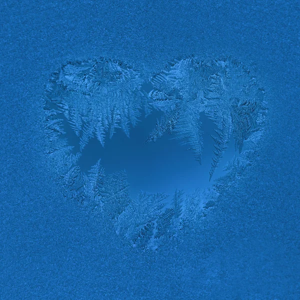 Christmas background in trendy color 2020 Classic Blue. Frosty window pattern in heart shape. Selective focus. — Stock Photo, Image