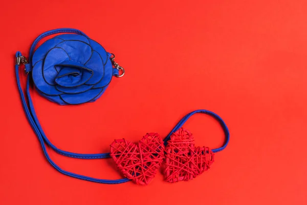 Ladies handbag in flower shape of color 2020 Classic Blue and two red braided hearts on red background.