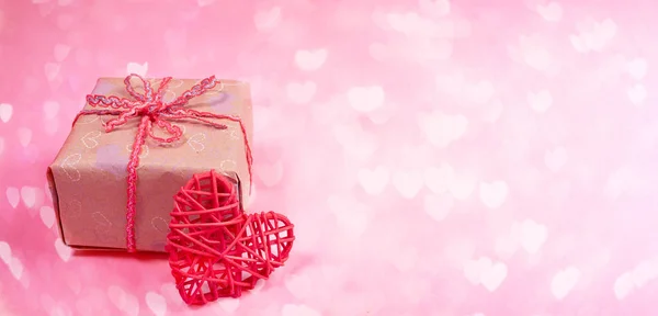 Valentinstag festliches rosa Banner mit diy verpackter Geschenkschachtel und rotem Weidenherz auf Bokeh-Hintergrund mit Herzen. — Stockfoto