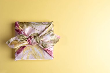 Sarı arka planda Japon Furoshiki tekniğine sarılı çiçek kumaşına sarılı bir hediye kutusu modası. Üst görünüm, alanı kopyala.