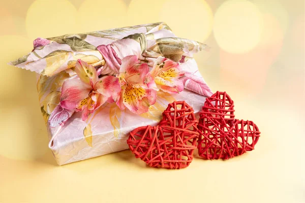 Тренді загорнута в техніку Фурошікі сувенірна коробка з квітами Альстроемія і двома червоними серцями хвіртки жовтого кольору з боке. — стокове фото