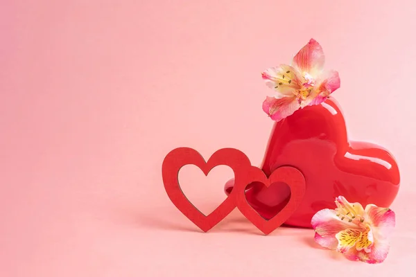 Rotes vasenförmiges Herz mit Blumen Alstroemeria und zwei rote Holzherzen auf rosa. Festlicher Hintergrund zum Valentinstag. — Stockfoto