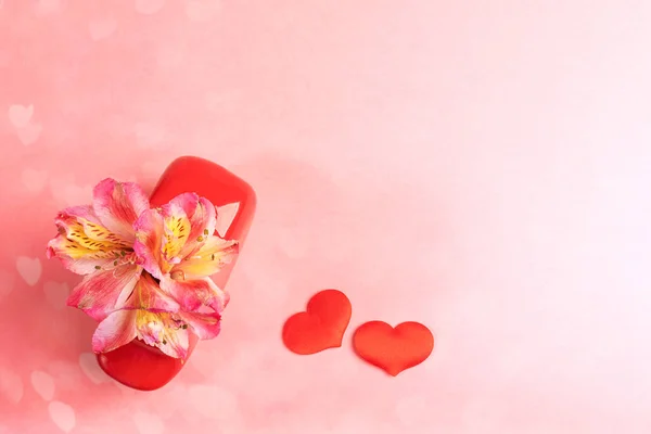Blumen Alstroemeria in roter Vase und zwei rote Textilherzen auf rosa Herzen Bokeh Hintergrund. Hintergrund zum Valentinstag. — Stockfoto