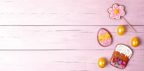 Festive Easter banner. Yellow eggs and colorful gingerbreads on pink wooden table. Copy space.