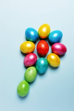 Paskalya 'nın yaratıcı kompozisyonu. Renkli Paskalya yumurtaları açık mavi pastel arka planda çiçek şeklinde serilmiştir. Üst manzara, düz yatış. Dikey yönelim.