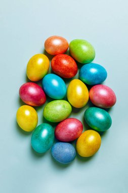 Paskalya 'nın yaratıcı kompozisyonu. Bir sürü renkli Paskalya yumurtası açık mavi pastel arka planda büyük bir Paskalya yumurtası şeklinde bırakıldı. Üst manzara, düz yatış. Dikey yönelim.