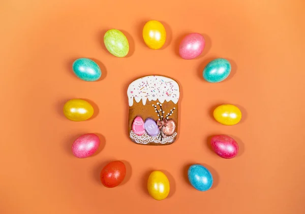 Color Easter eggs laid out in circle and gingerbread Easter cake in center on orange background. Festive Easter layout.