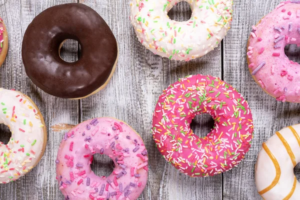 Donuts tradicionales con esmalte multicolor dispuestos sobre fondo de madera pintado blanco de cerca . —  Fotos de Stock