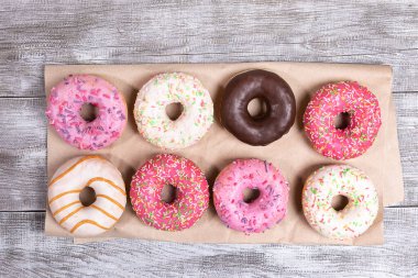 Çok renkli jöleli sekiz geleneksel donut beyaz boyanmış ahşap arka planda ambalaj kağıdına güzelce serilmiş. Donut - geleneksel tatlı pasta. Üst manzara, düz uzanma.