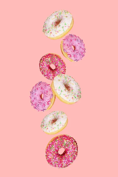 用五颜六色的釉料在时髦的粉色背景上掉落甜甜圈 甜甜圈是传统的甜糕点 创意食品趋势 征收食物 纵向方向 — 图库照片