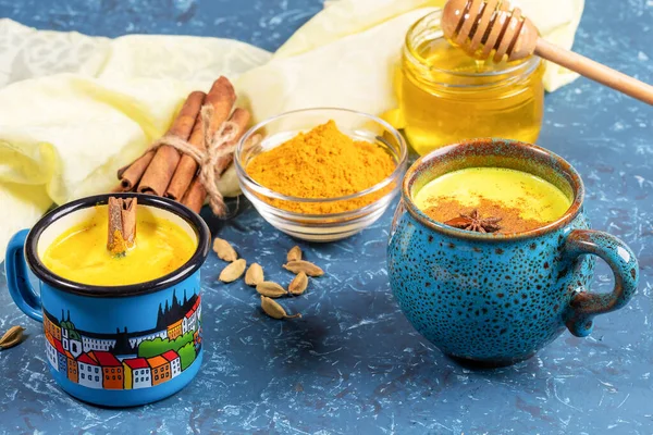 Sarı peçetede pişmesi için iki mavi fincanda altın zerdeçal sütü ve malzeme. Mavi fon. Altın zerdeçal sütü - bağışıklığı geliştirmek için organik ayurvedik sağlıklı içecek. Seçici odak.