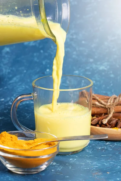 Leite de açafrão orgânico. Corrente de leite dourado está fluindo em vidro de decantador e ingredientes em fundo azul . — Fotografia de Stock