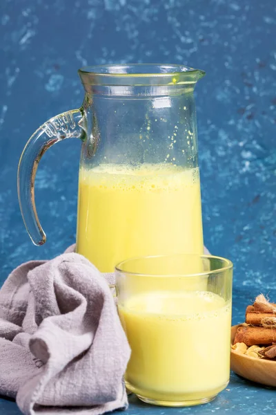 Leite de açafrão orgânico. Decantador e vidro com leite dourado, guardanapo e ingredientes em fundo azul . — Fotografia de Stock