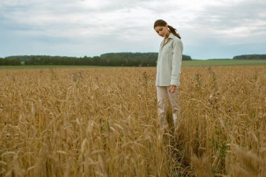 İnce, kahverengi saçlı güzel bir kadın buğday tarlasında yürüyor..