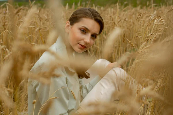 Mooi Slavisch meisje in licht kleren zitten in een tarwe veld. — Stockfoto