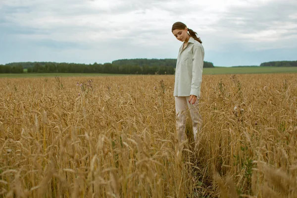 İnce, kahverengi saçlı güzel bir kadın buğday tarlasında yürüyor..