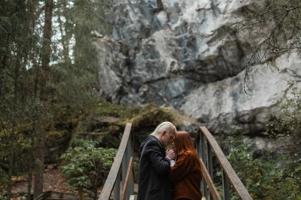 Una pareja enamorada en el bosque se coge de la mano contra el telón de fondo de una roca —  Fotos de Stock