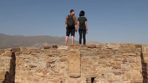 Ein junges Paar steht an der Mauer eines alten Schlosses und blickt auf die Stadt — Stockvideo