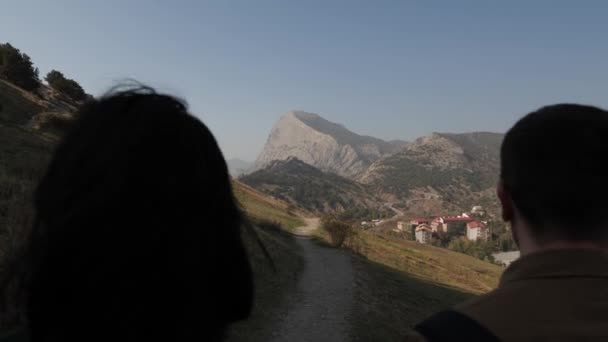 Bir çift genç insan, dağların arka planında yürür. — Stok video